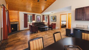 A spacious living room with a fireplace, wooden ceiling, and a dining area with a table and chairs.