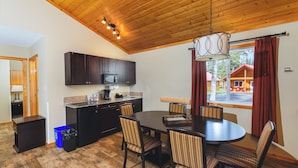 A modern kitchen with dark cabinets, a microwave, and a sink. There is a dining area with a wooden table and chairs.