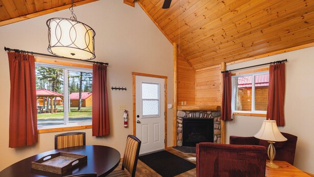 A cozy room with a fireplace, wooden ceiling, and large windows with curtains. - Single Bedroom Unit in the Mountain (Jasper east)