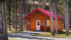 A wooden cabin with a red roof, a front door, and a small porch with two chairs. - Single Bedroom Unit in the Mountain (Jasper east)