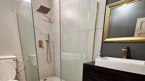 Un baño moderno con ducha de vidrio, inodoro blanco y tocador de madera oscura con espejo.