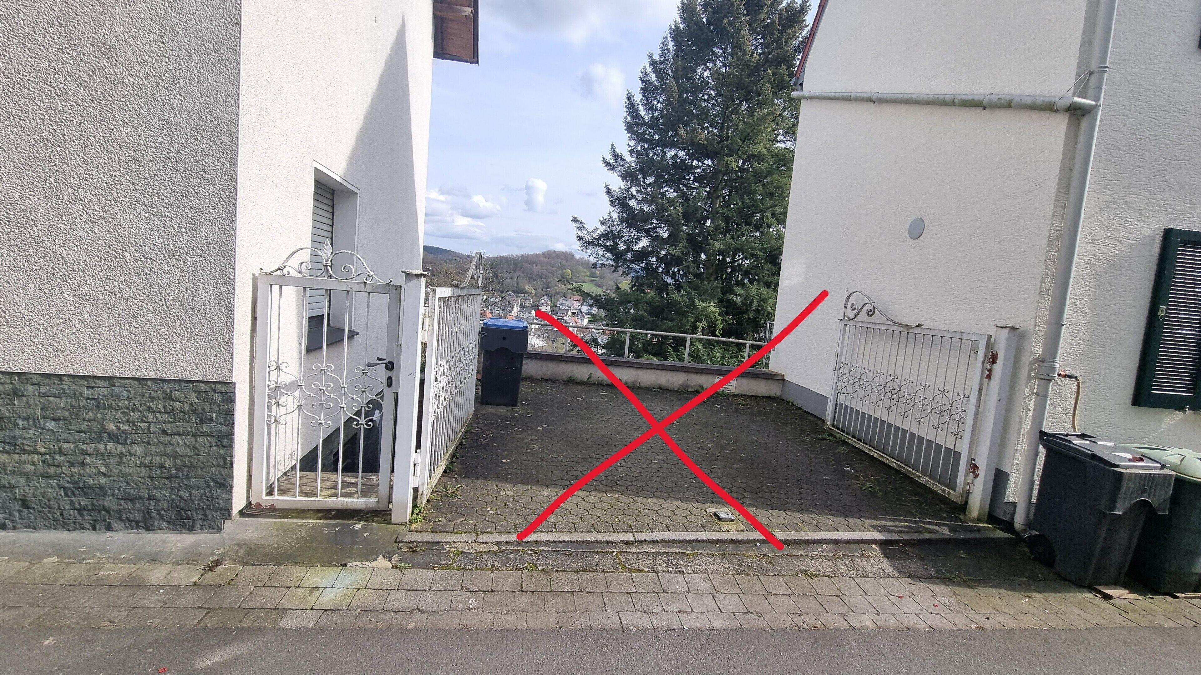 A narrow alleyway with a gated entrance, a trash bin, and a metal fence.