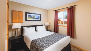 Habitación de hotel con una cama, dos mesitas de noche con lámparas, un cuadro en la pared y una ventana con cortinas.
