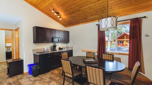 Una cocina moderna con armarios oscuros, un microondas y un lavamanos. Hay una zona de comedor con una mesa y sillas de madera.