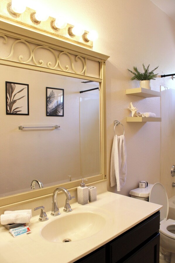 A bathroom with a large mirror, a sink, a toilet, and a shelf with a plant. - Charming 3-bed w/Pool near State Farm Stadium and Mattel Adventure Park (Glendale)