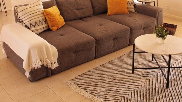 Ein Wohnzimmer mit einem Ecksofa, einem runden Couchtisch, einem Deckenventilator und einem Essbereich mit einem roten Tisch und Stühlen.