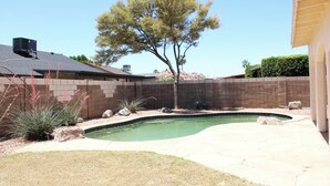 Ein Garten mit Swimmingpool, Baum und Backsteinmauer.