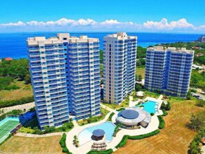 A high-rise hotel complex with multiple floors, a swimming pool, and a tennis court.