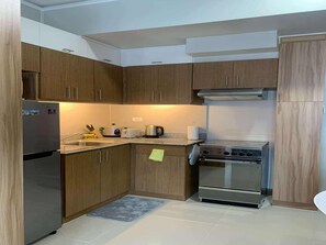 A compact kitchen with wooden cabinets, a stainless steel refrigerator, a stove, and a sink. - Amisa Private Residences Tower C (Lapu-Lapu)