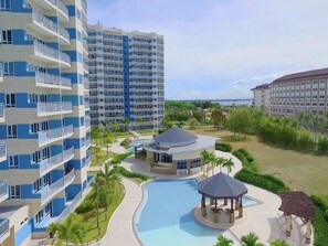 Un hôtel de grande hauteur doté de nombreux balcons, d’un espace piscine central agrémenté d’un kiosque et offrant une vue sur la mer.