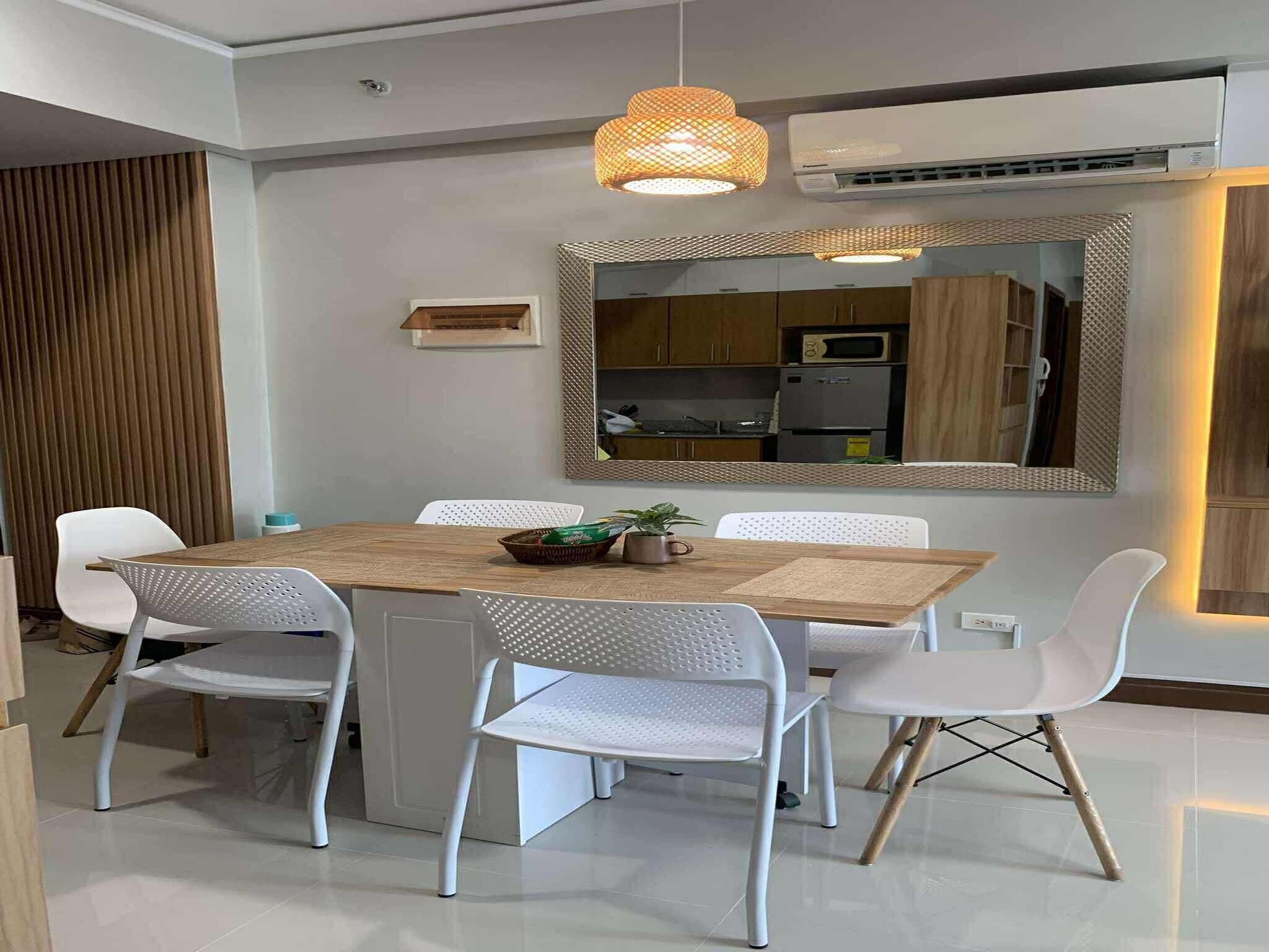 Un espace repas moderne avec une table en bois, des chaises blanches et un grand miroir au-dessus.