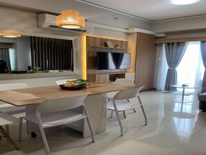 A modern dining area with a wooden table, white chairs, a TV, and a decorative hanging light fixture. - Amisa Private Residences Tower C (Lapu-Lapu)