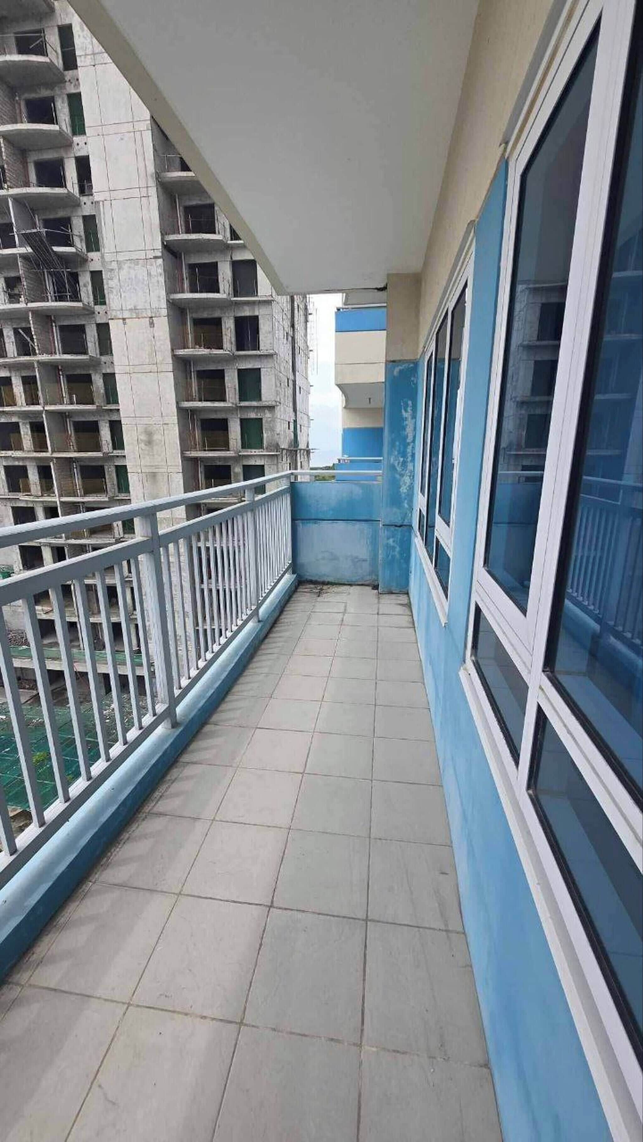 A corridor with tiled flooring, a white railing, and large windows on one side.