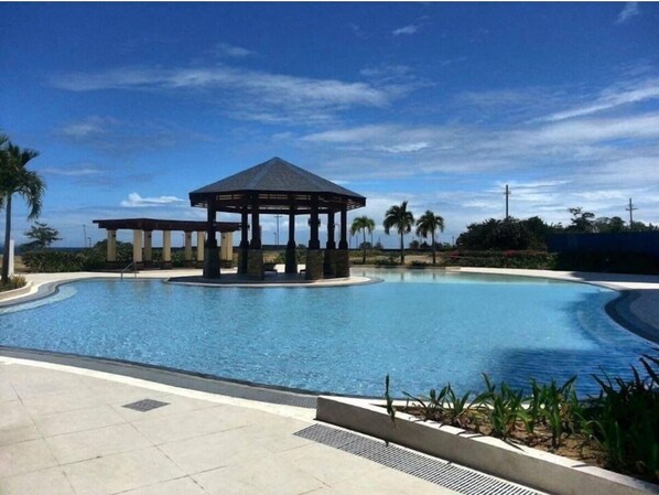 A pool with a gazebo, palm trees, and a clear sky.