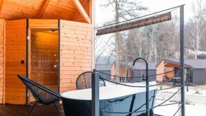 Una cabaña de madera con un jacuzzi en una terraza, rodeada de árboles.