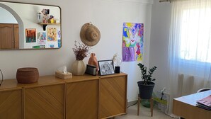 Un salon moderne avec un meuble en bois, un miroir, une plante en pot et un tableau coloré accroché au mur.