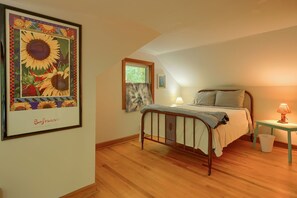 Un dormitorio con cama, mesita de noche, lámpara, un cuadro enmarcado y ventana con cortinas.