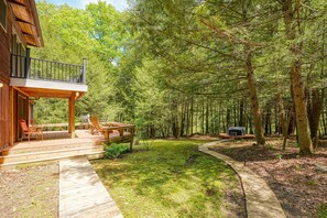 A wooden cabin with a deck and outdoor seating area surrounded by a dense forest.