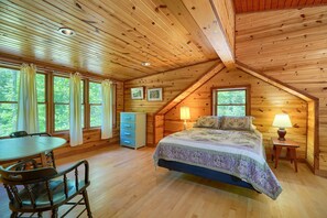 A wooden cabin bedroom with a bed, a desk, and a chair.