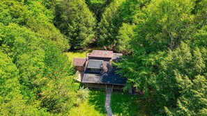 A house surrounded by dense forest, with a visible deck and a small porch.