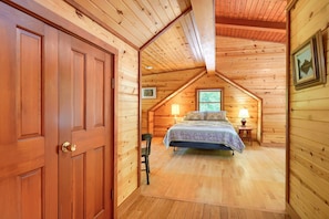 Un dormitorio acogedor tipo cabaña de madera con una cama, una silla y una mesita de noche con lámpara.