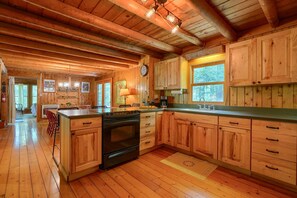 Een ruime keuken met houten kastjes, een centraal keukenblok en een groot raam voor veel daglicht.