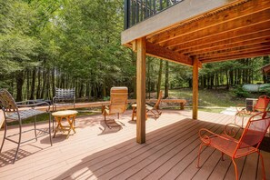 Una terraza de madera con mobiliario exterior, rodeada por un bosque.