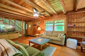 Interior acogedor de una cabaña con techo de madera, un televisor, un sofá, una mesa de centro y una estantería.