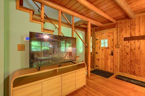 Un interior de madera con un televisor de pantalla plana grande sobre un mueble de madera, un termostato y una puerta de madera.