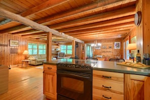 Una cocina amplia con armarios de madera, una isla grande y un horno empotrado. Hay un comedor con mesa y sillas, y una sala de estar con sofá y lámpara.