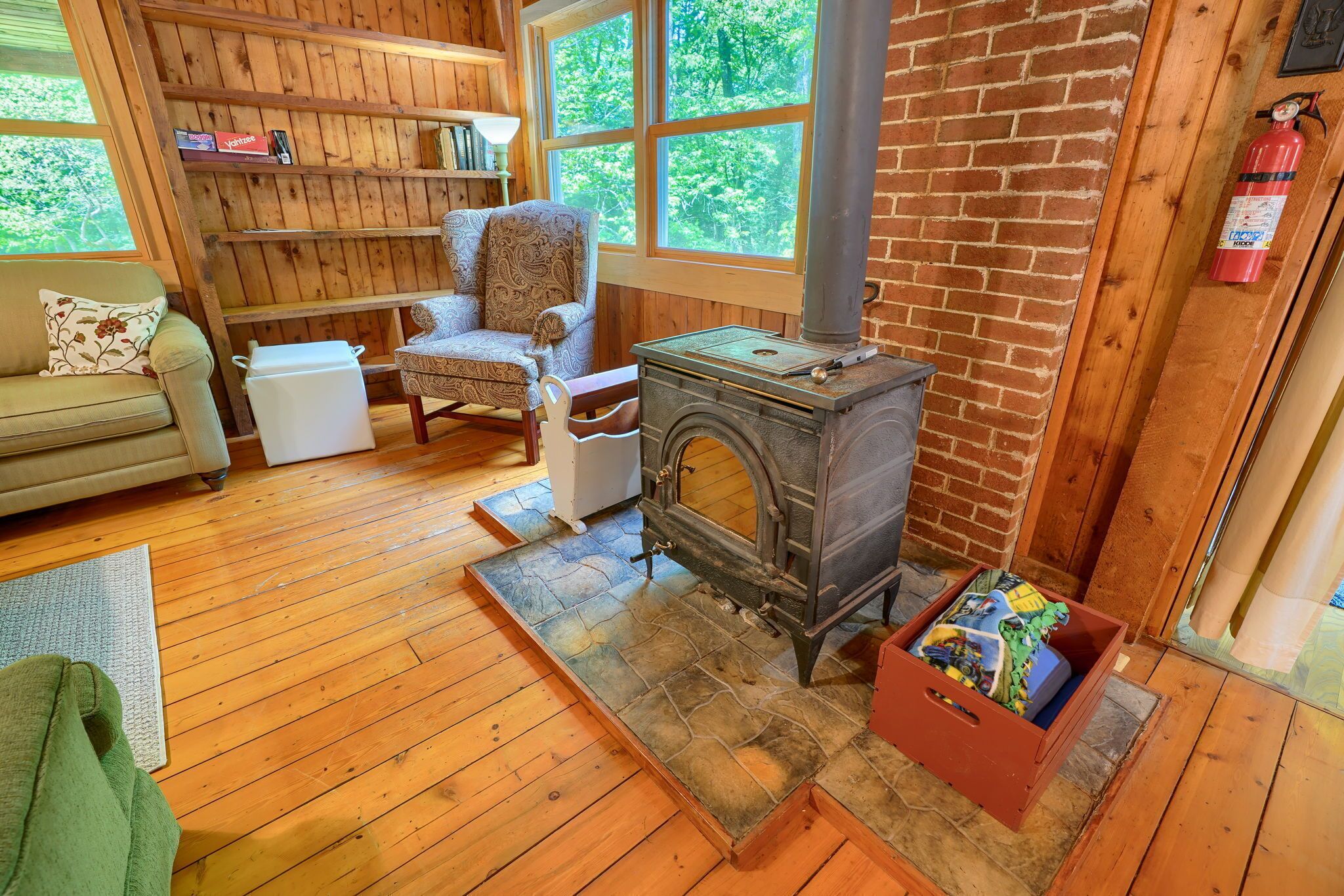 A cozy room with a wooden floor, a sofa, a patterned armchair, a small table, a fireplace, and a bookshelf.