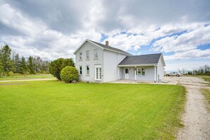 Ett vitt hus i två våningar med ett garage, omgivet av en välskött gräsmatta och en grusuppfart.