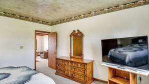 A bedroom with a bed, dresser, TV, and a door leading to another room. - Manitowoc Lakefront Home on 15 Acres: Dogs OK! (Manitowoc)