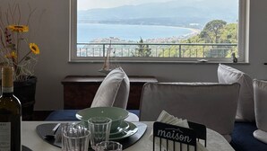 A dining table with plates, glasses, and a bottle of wine, set against a scenic view of a lake and mountains. - Maison Stalettì between sky, sea and prickly pears (Lucerta)