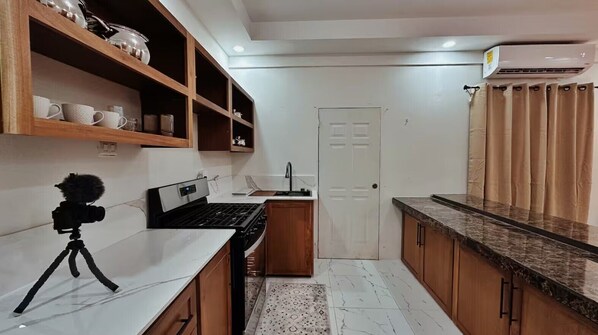 Una cocina con armarios de madera, una estufa, una cámara sobre un trípode y una puerta blanca.