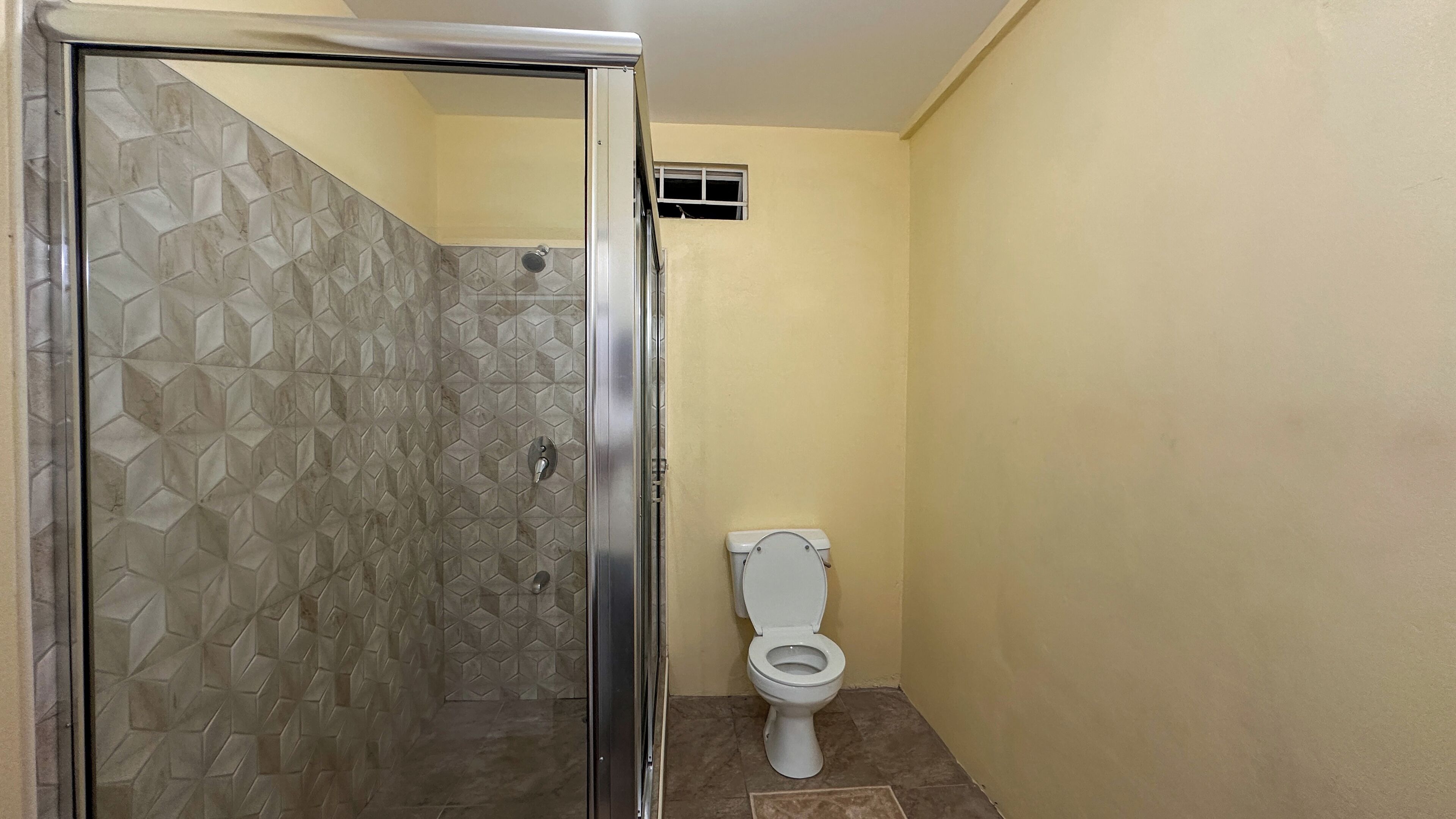 Un bagno con zona doccia caratterizzata da piastrelle a motivi geometrici e un water con sedile e coperchio bianchi.