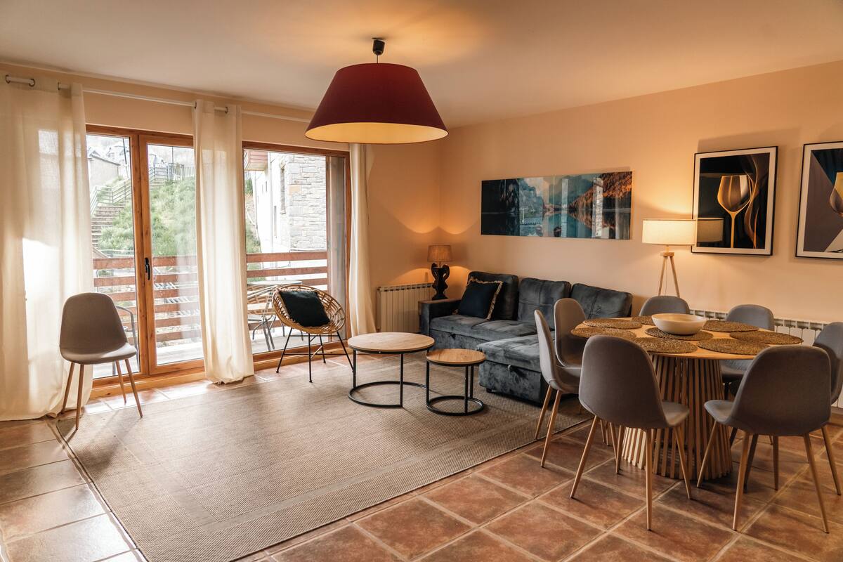 A modern living room with a sofa, dining table, chairs, and a large window with curtains.