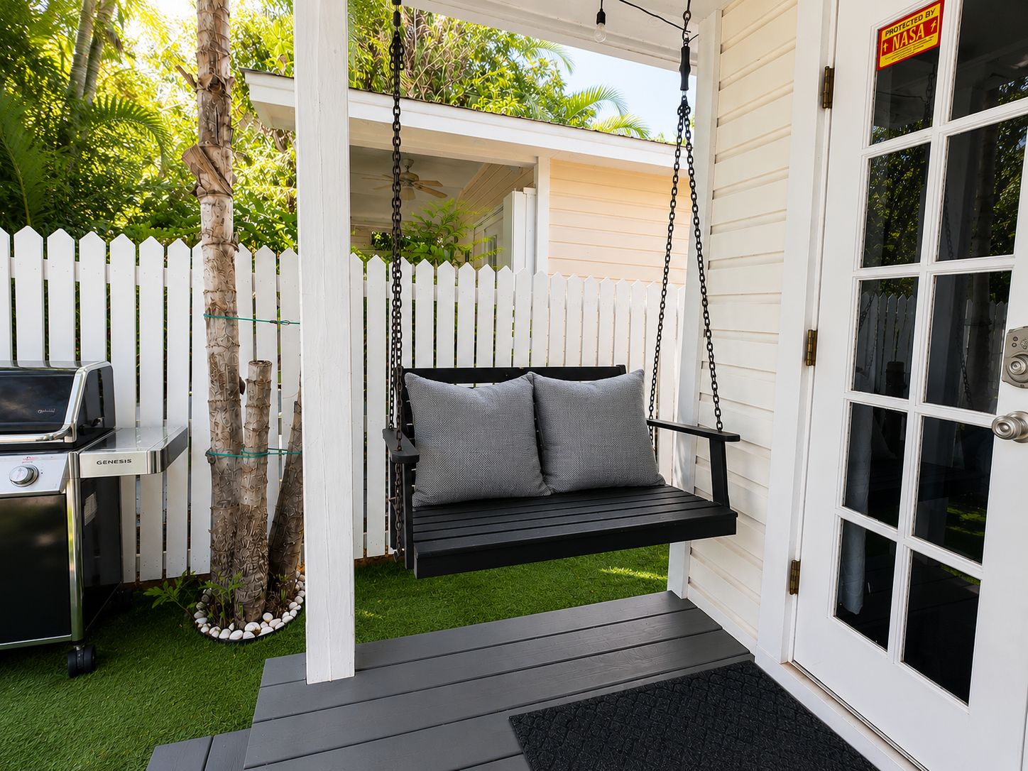 A porch with a swing, a grill, and a white picket fence.