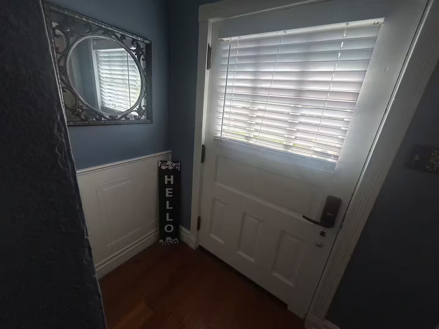 Un pasillo con una puerta blanca, un espejo decorativo y un cartel que dice 'HELLO'.