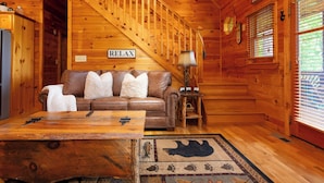 L'intérieur d'un chalet en bois, avec un canapé en cuir marron, une table basse en bois et un panneau mural portant l'inscription « RELAX ».