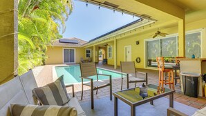 A poolside area with a yellow wall, a pool, and outdoor furniture including a sofa and chairs. - 5 Mi to Jupiter Beach Park: Poolside Oasis! (Jupiter)