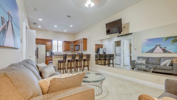 A spacious living area with a sofa, a glass coffee table, and a dining area with wooden chairs and a TV. - 5 Mi to Jupiter Beach Park: Poolside Oasis! (Jupiter)