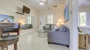 A spacious living area with a gray sofa, a glass coffee table, and a wooden chair. A television is mounted on the wall, and there is a door leading to another room. - 5 Mi to Jupiter Beach Park: Poolside Oasis! (Jupiter)