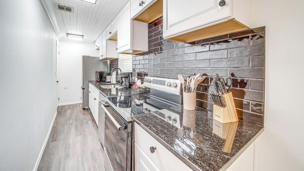 A modern kitchen with white cabinetry, a granite countertop, and a backsplash with gray tiles. - Waterfront Lake Eufaula Home: Dock & Beach Access! (Eufaula)