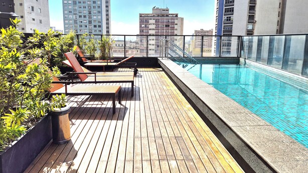 Un espace piscine aménagé sur le toit, avec une terrasse en bois, des chaises longues et une vue sur les bâtiments environnants.