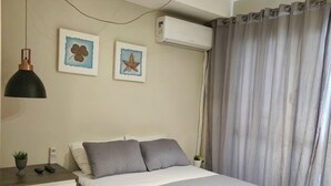Une chambre à coucher comprenant un lit, une table de chevet, une lampe, un appareil de climatisation et des rideaux.