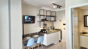 Une cuisine moderne dotée d’un téléviseur à écran plat, de meubles blancs et de chaises bleues.