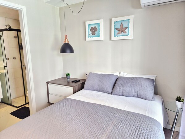Un dormitorio con cama, mesita de noche, lámpara y dos cuadros en la pared.