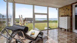 Un balcón con vistas a un lago, una silla de mimbre, una mesa con una revista y un mueble blanco.