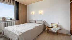 Un dormitorio con una cama grande, una ventana con vistas, una mesita de noche con una lámpara y un globo terráqueo en el alféizar.